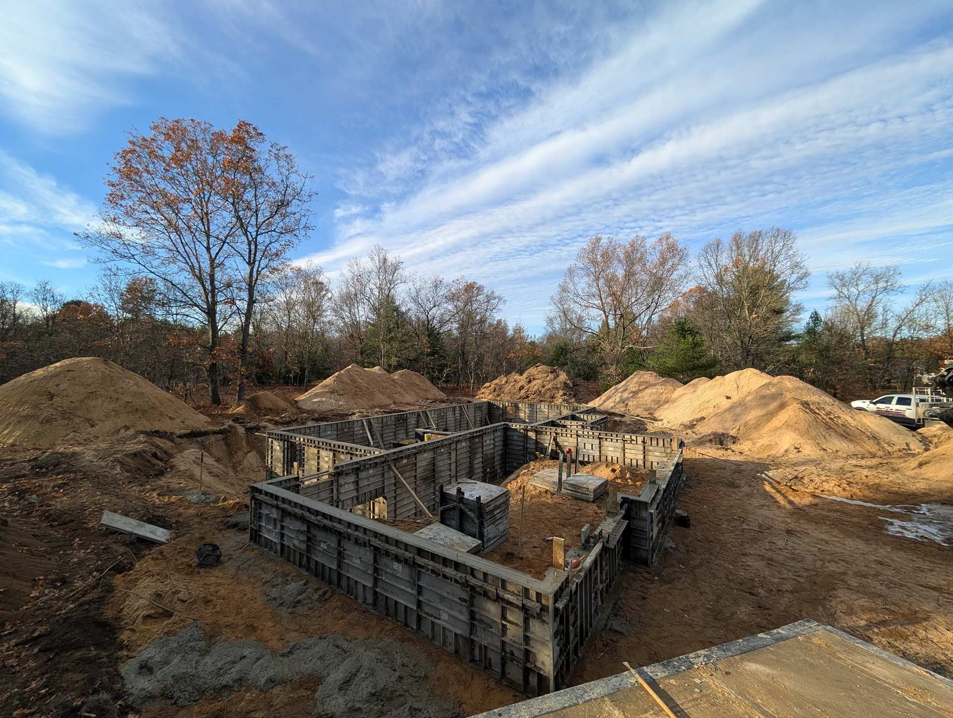 Concrete foundation forms for a new house under construction in a wooded area with piles of dirt surrounding the site.
