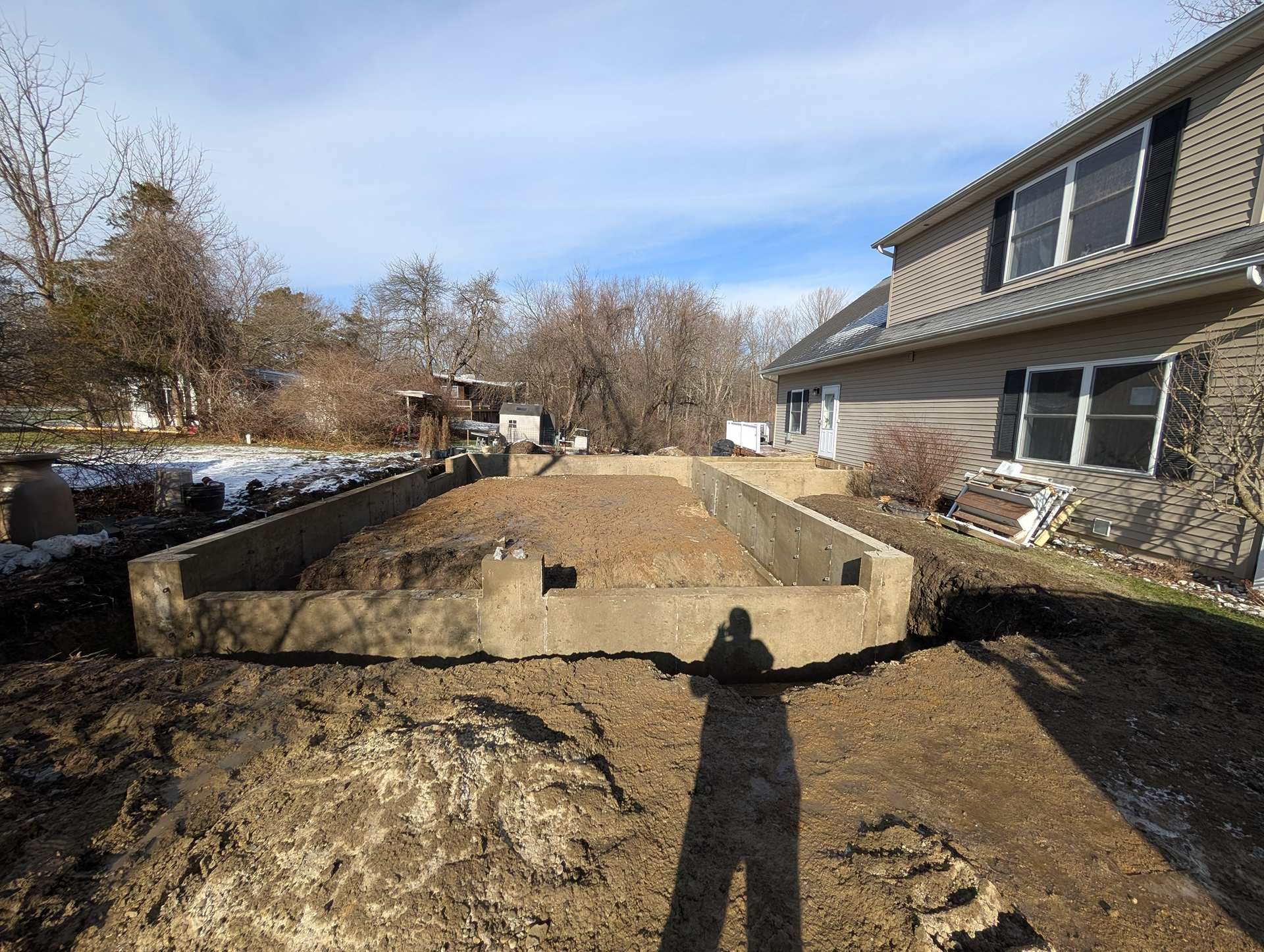 An outdoor view of a concrete foundation for a new structure being built next to the side of a house.