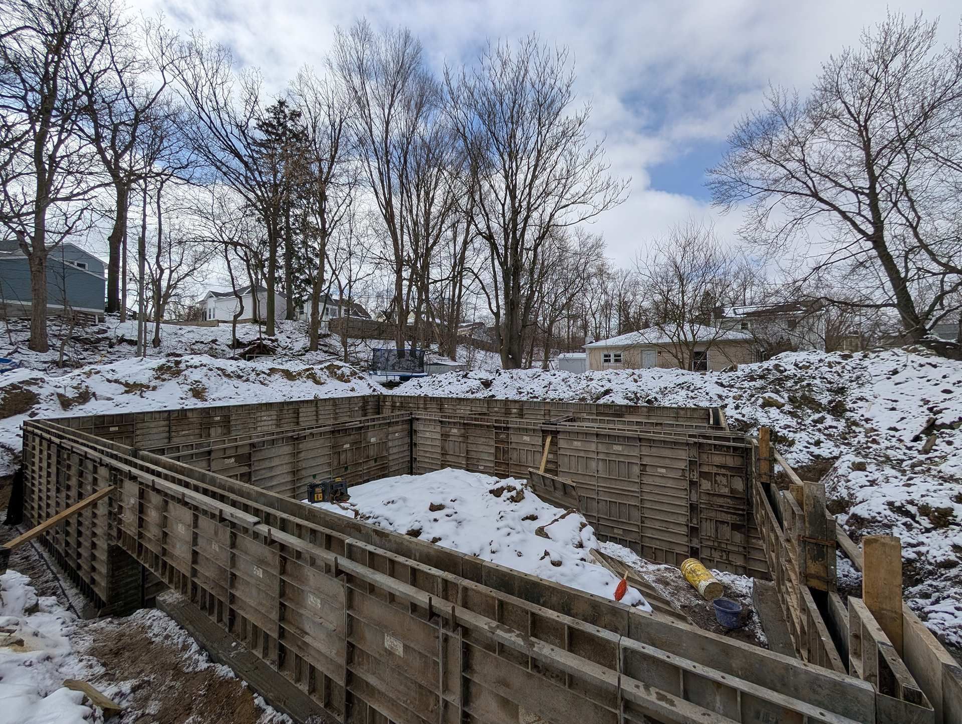 Concrete foundation walls in wooden forms set in a snowy, wooded construction site.