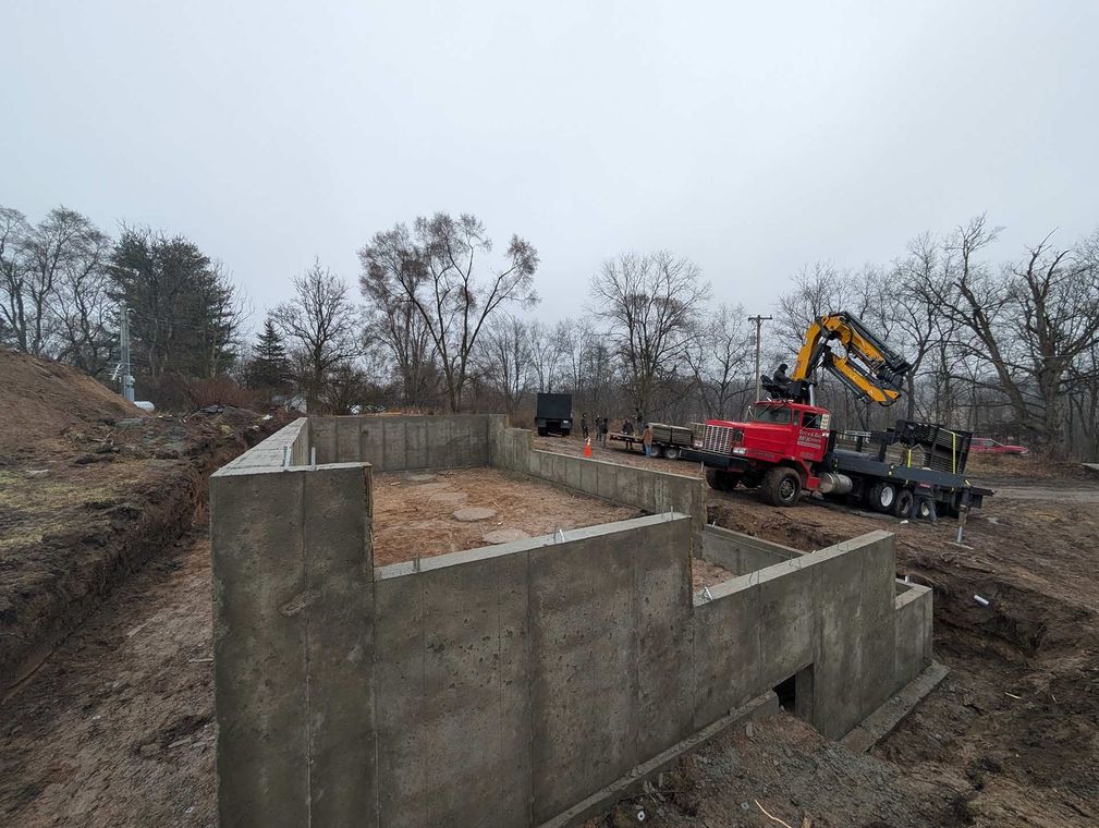A red crane sits at a construction site with a freshly poured concrete foundation for a new building.