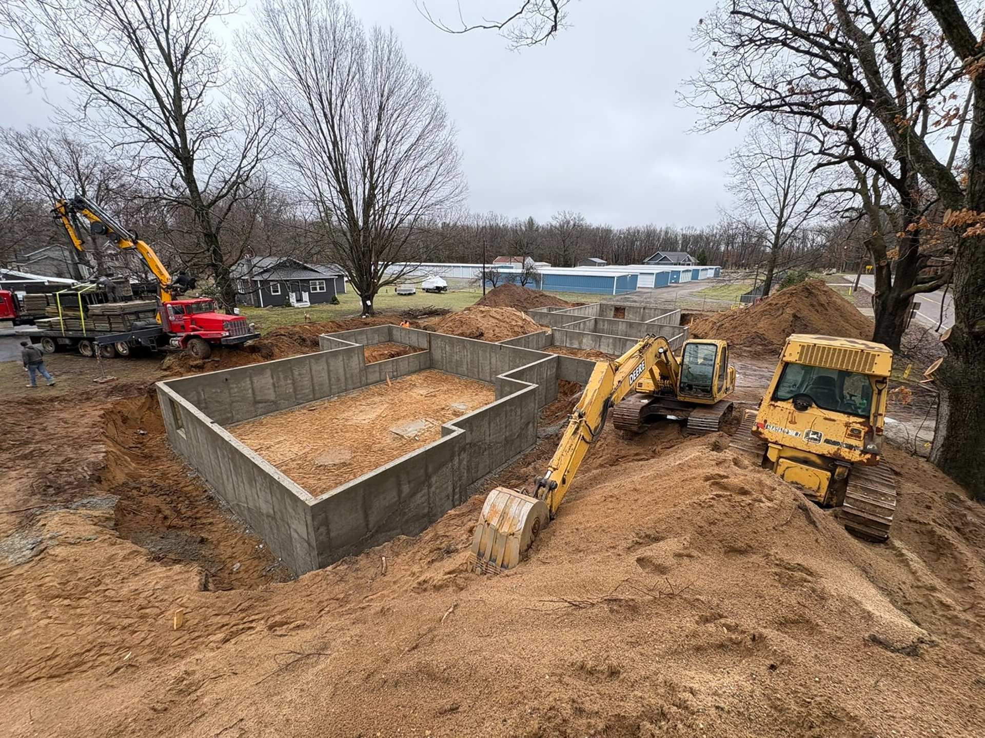 An active construction site with a concrete foundation, yellow excavators, and a red truck on a dirt lot.