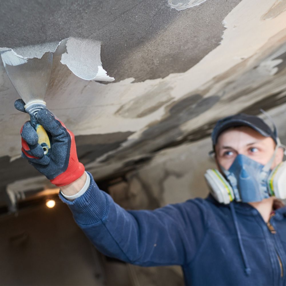 A man wearing a mask and gloves is working on a ceiling