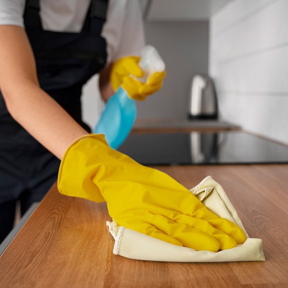 A person wearing yellow gloves is cleaning a wooden counter top with a cloth.