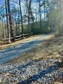 Gravel path beside a wooden fence in a wooded area with bare trees and sunlight filtering through