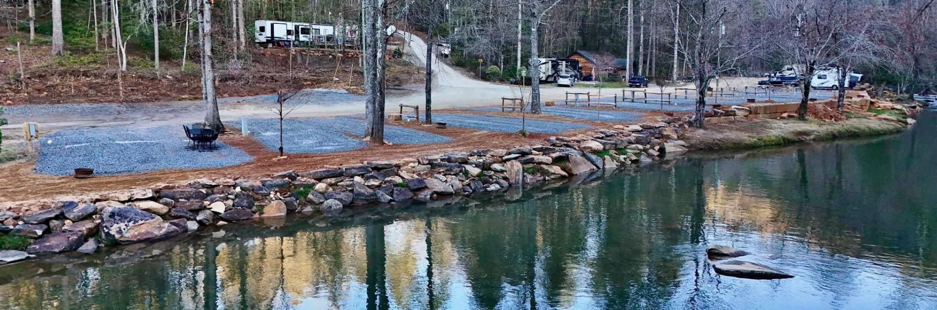 Rock-lined pond edge with winter trees, a small dock, and a fountain spraying in the water