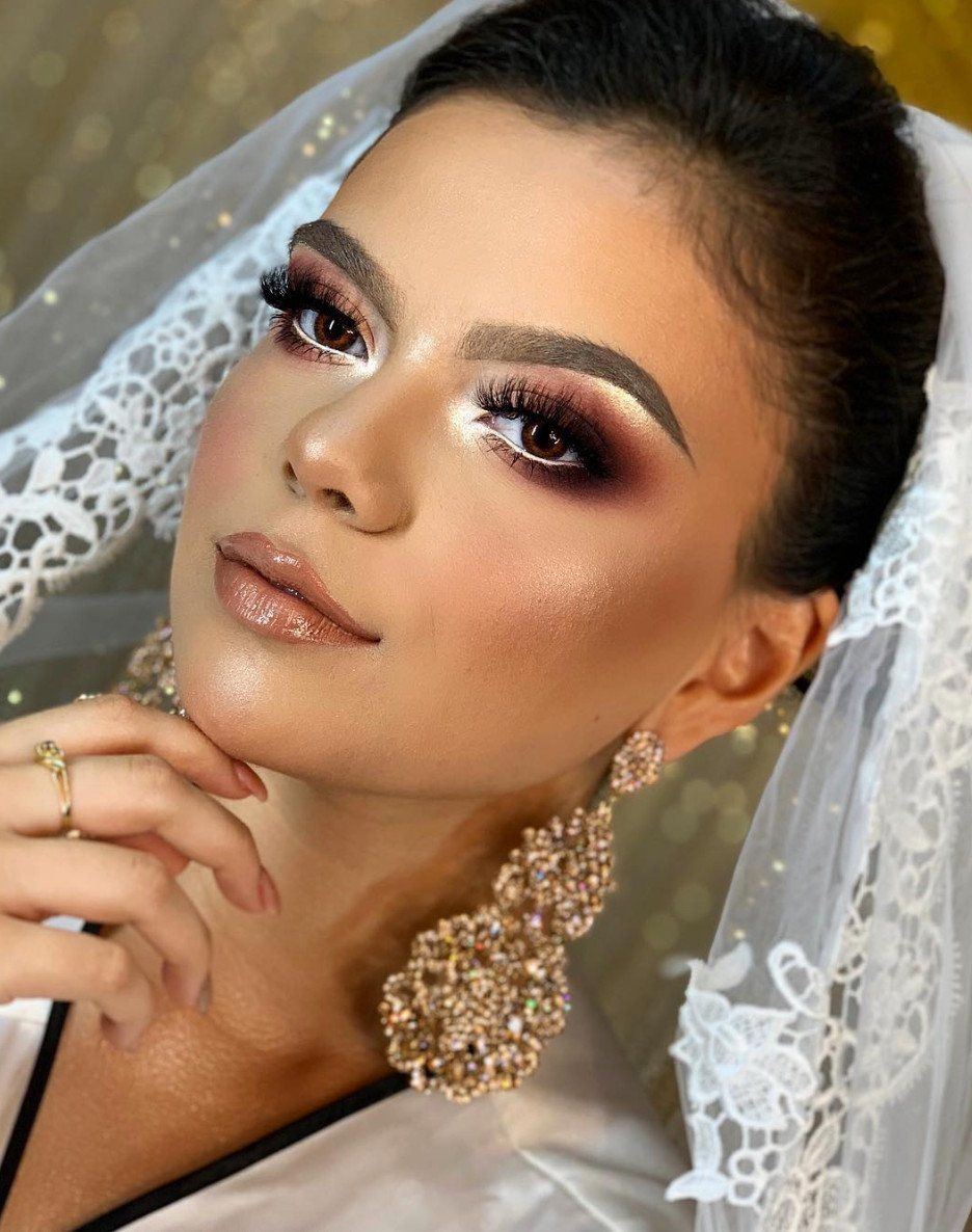 Donna con trucco glamour, che indossa un velo e grandi orecchini d'oro, che si tocca il mento.