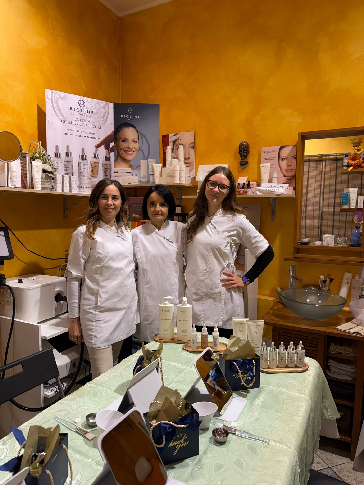 Due donne assistono un cliente al bancone di un negozio, circondate da espositori di prodotti e opere d'arte incorniciate.