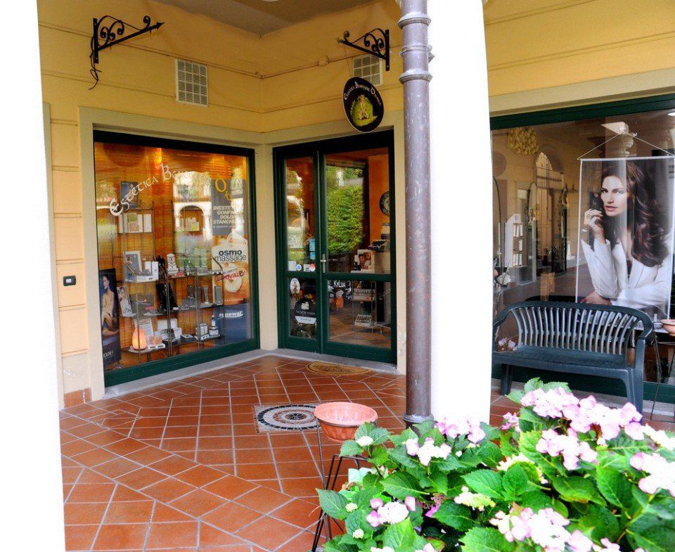 Esterno di un negozio con porte e finestre con cornici verdi, fiori in vaso e un patio in mattoni.
