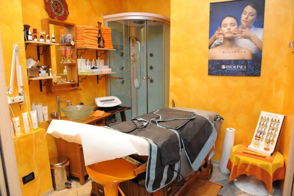 Sala per massaggi terapeutici con pareti arancioni, lettino per massaggi, doccia, prodotti per la cura della pelle.