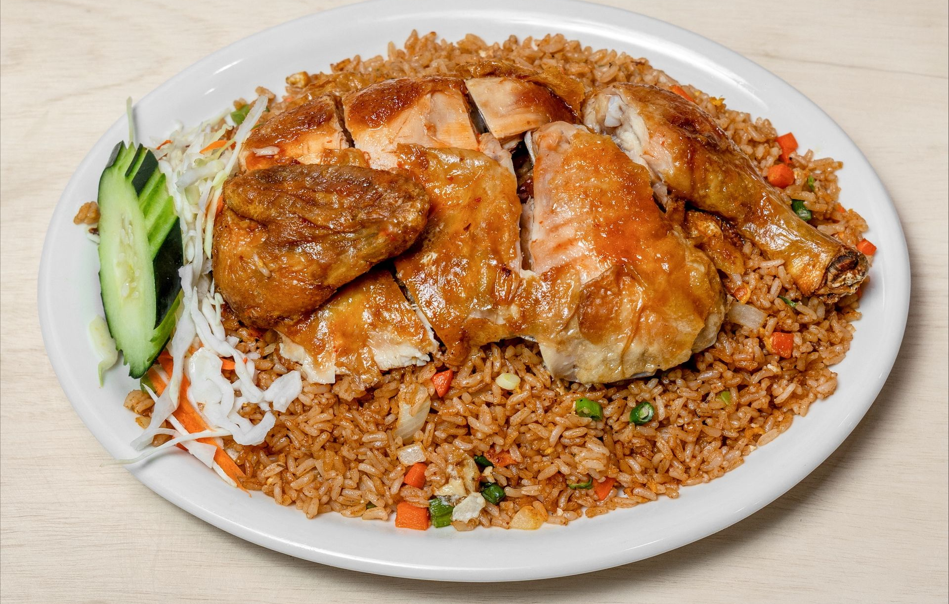 Roasted chicken on a bed of fried rice, served with cucumber slices and shredded cabbage on a white plate.