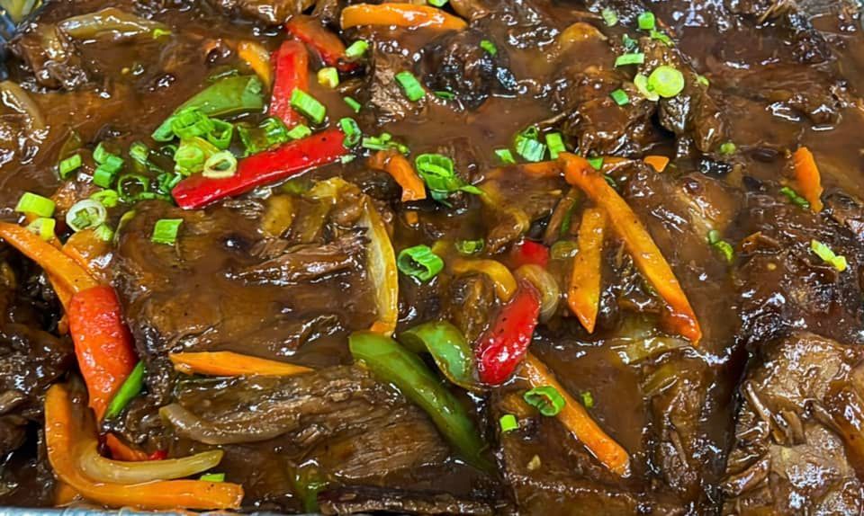 Beef dish with a dark brown sauce, colorful peppers and carrots.