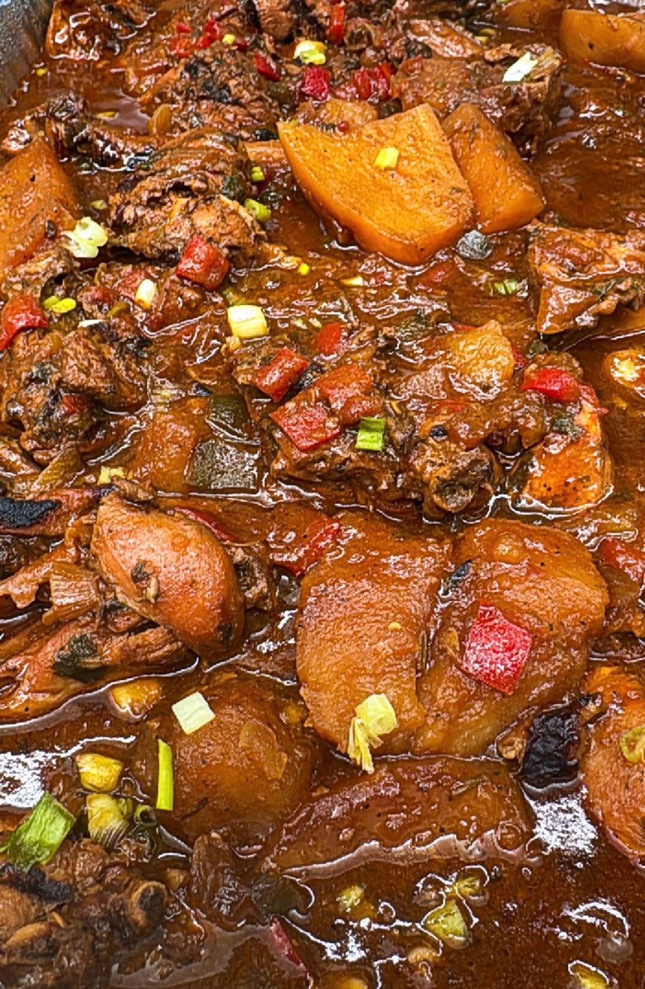 Chicken and potato stew, brown sauce, garnished with red peppers and green onions.