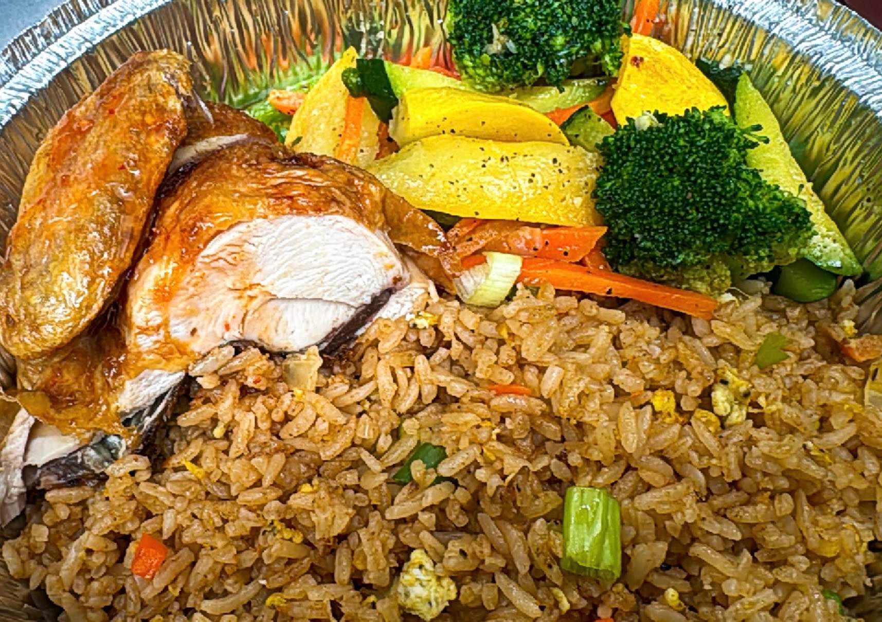 Chicken and fried rice meal with vegetables in a foil container.