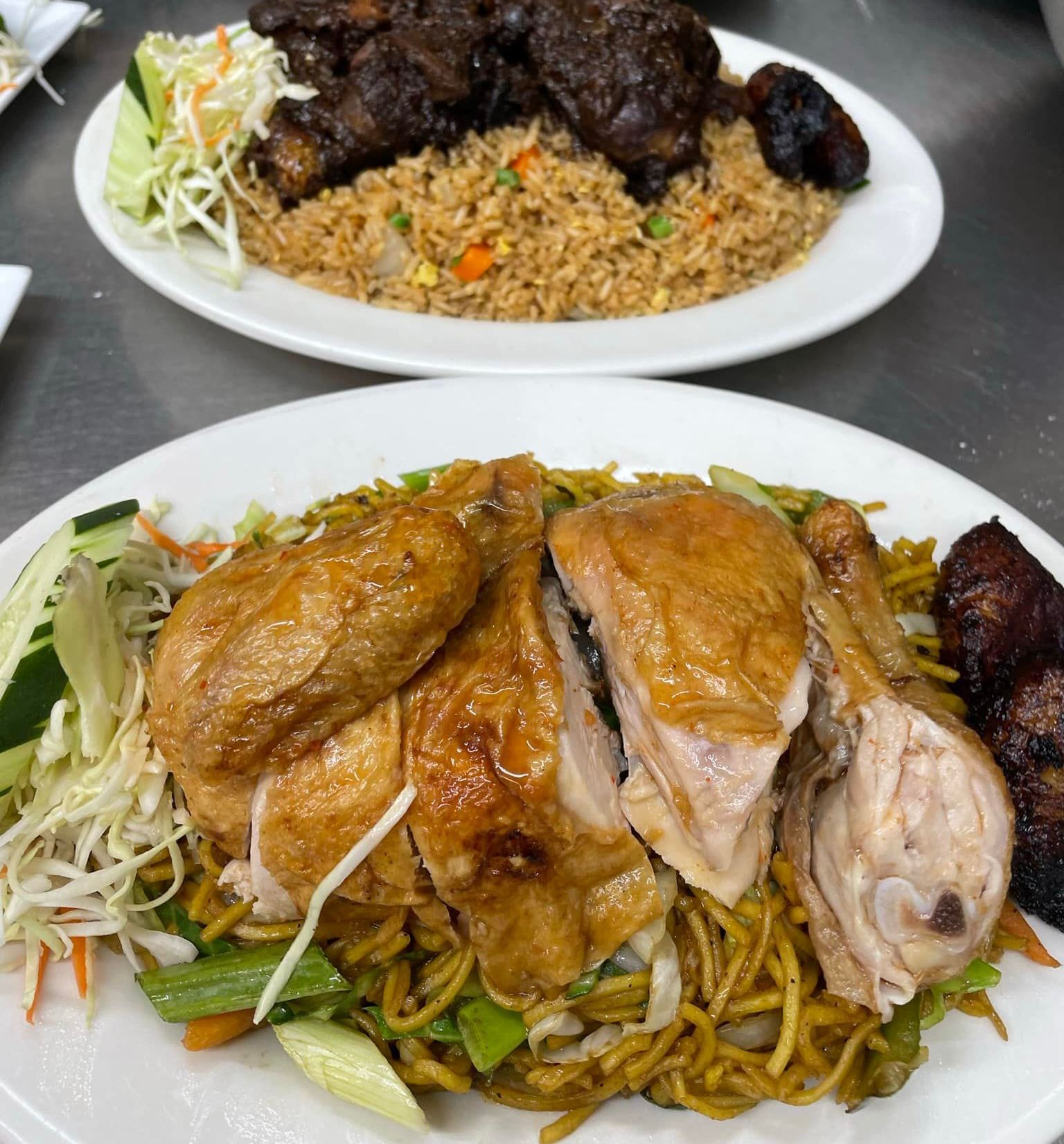 Plates of cooked chicken and meat with fried rice or noodles, garnished with vegetables, arranged on a table.