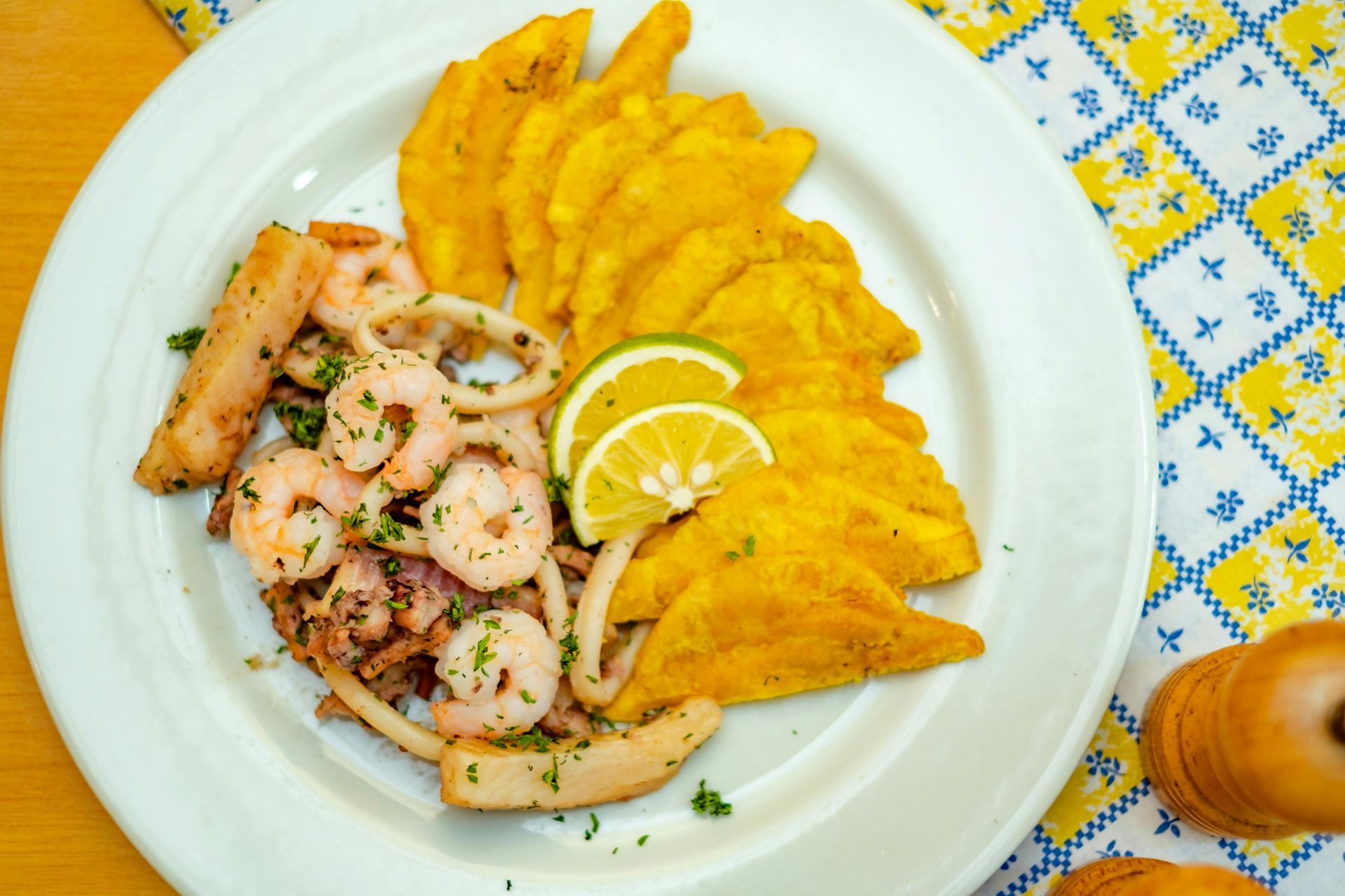 Seafood dish with fried plantains, lime slices, and parsley garnish on a white plate.