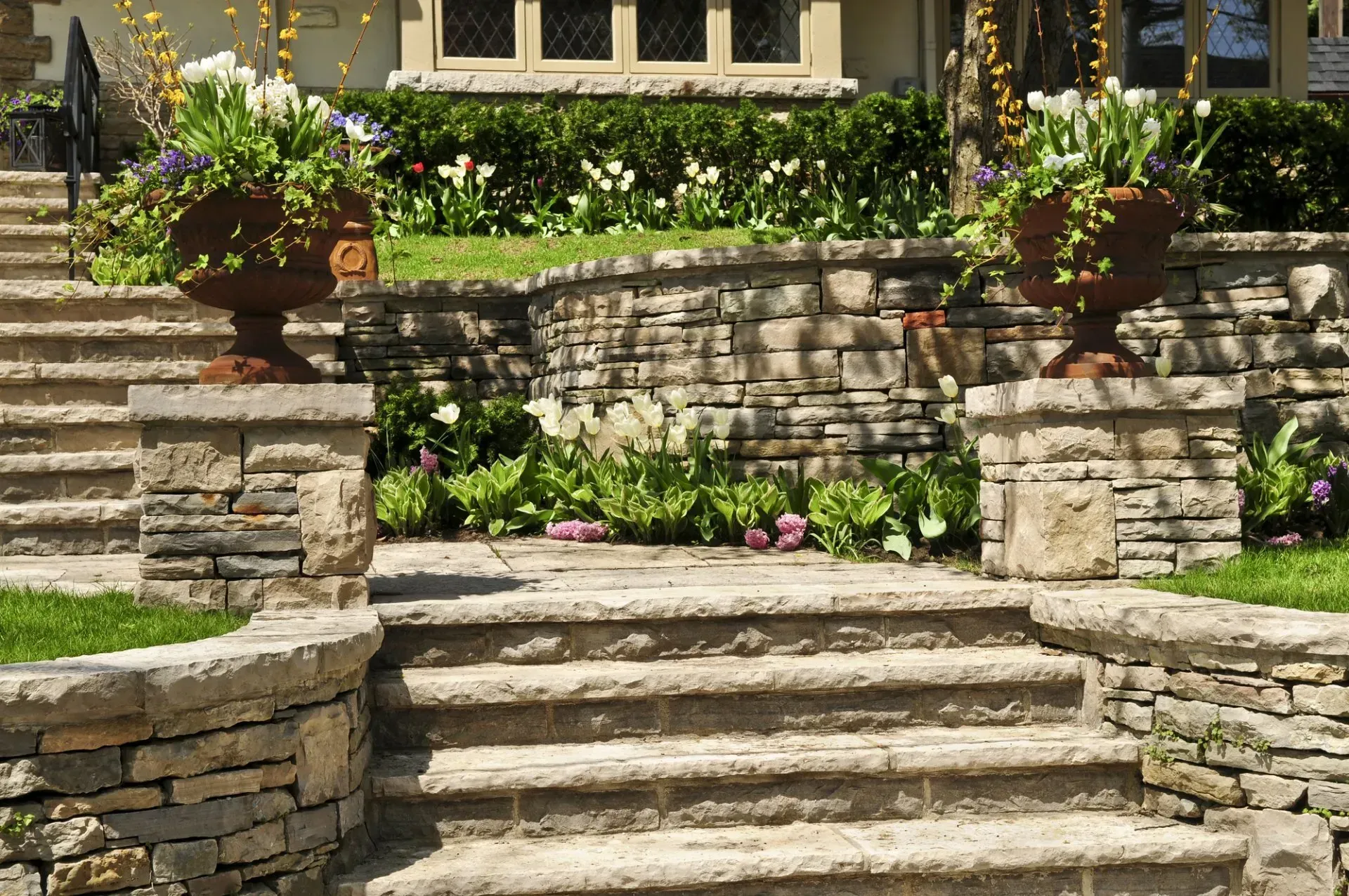 Stone steps leading up to a house with planters and greenery.