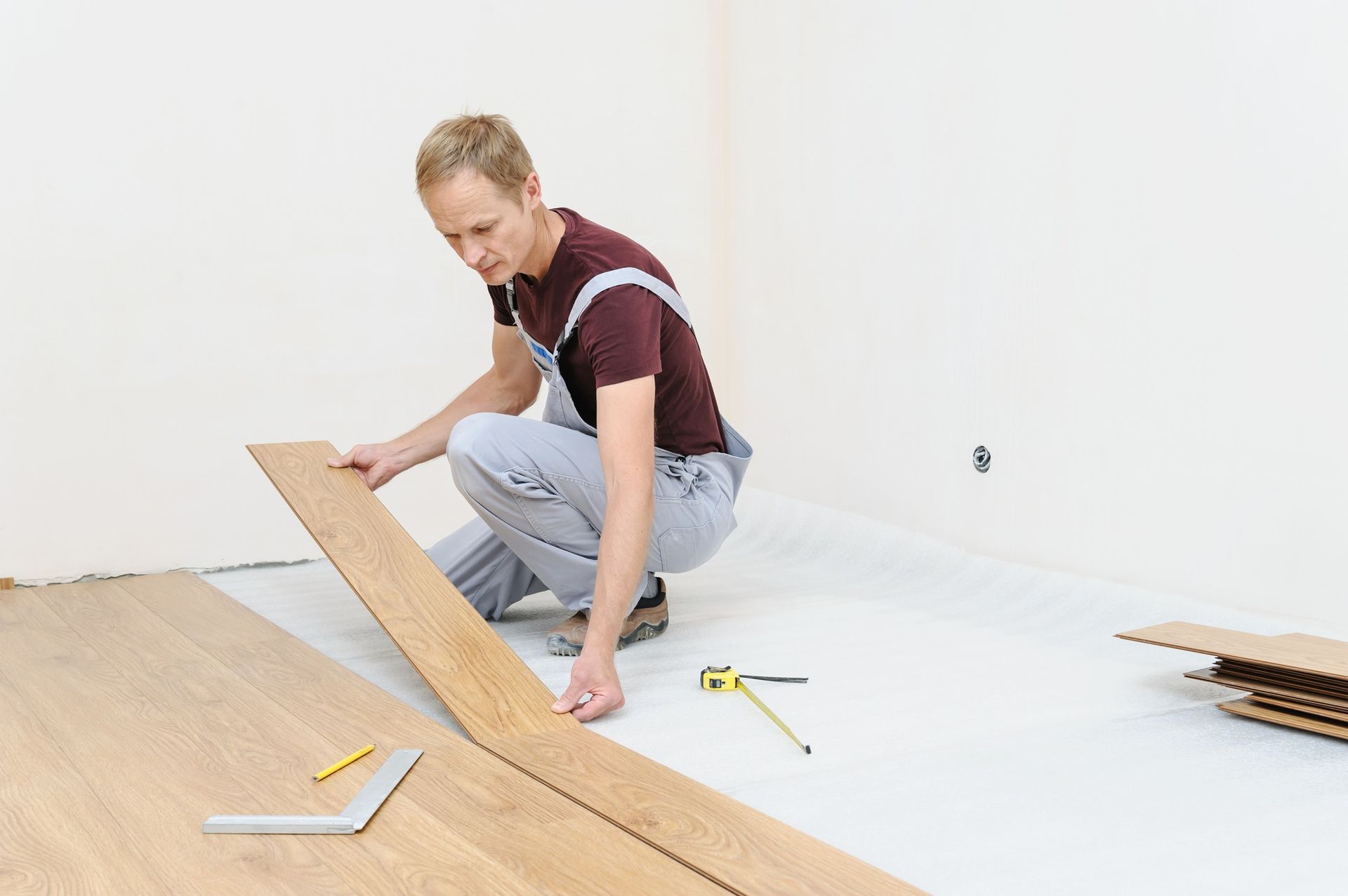 Man installing laminate flooring in empty room with tools, DIY home renovation project setup.