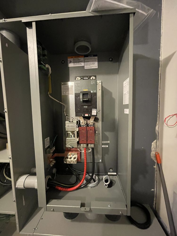 Metal electrical panel with circuit breaker, wires, and other components. Gray cabinet with black and red wiring.