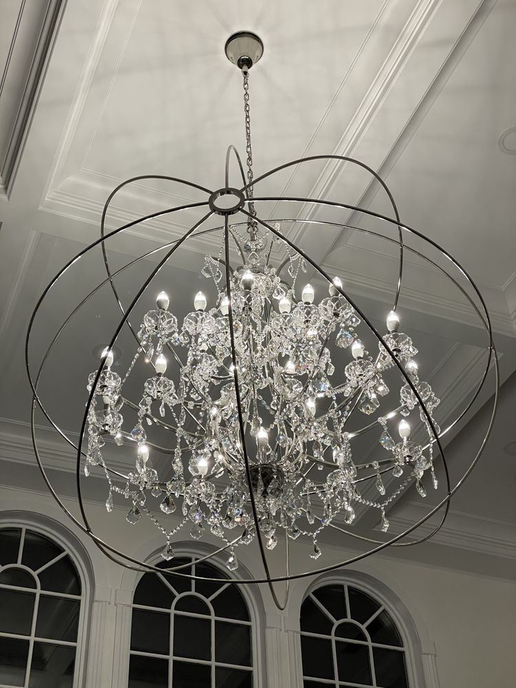 Ornate crystal chandelier suspended from a patterned ceiling. Metal frame surrounds the lights.