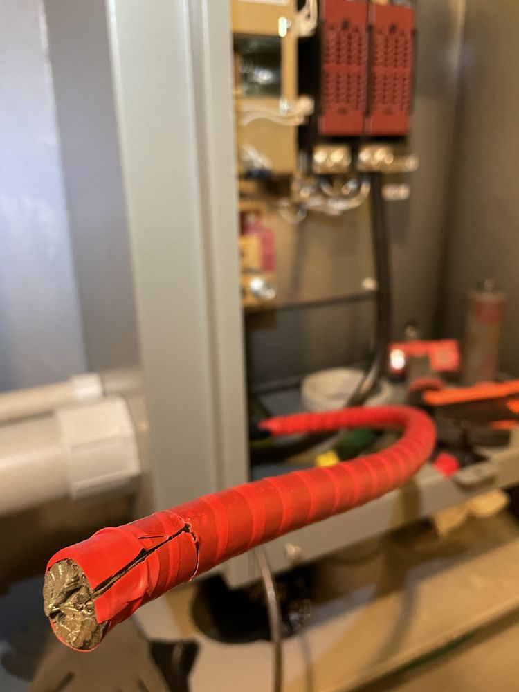 A red electrical wire with a stripped end, coiled and sitting near a gray electrical panel.