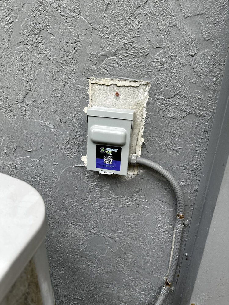 Gray electrical box mounted on a textured gray wall, connected by a conduit.