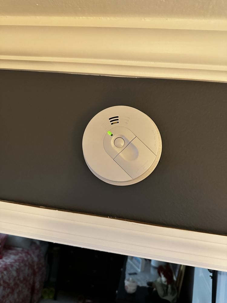 White smoke detector with a green light on a gray wall.