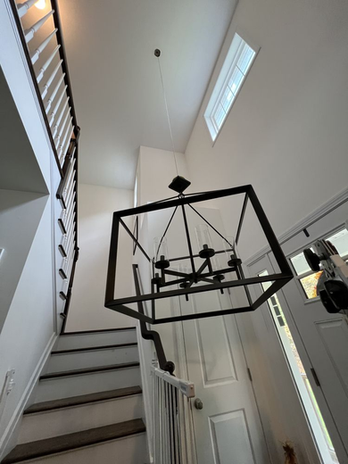 Entryway with staircase, large black chandelier, white walls, and a window.