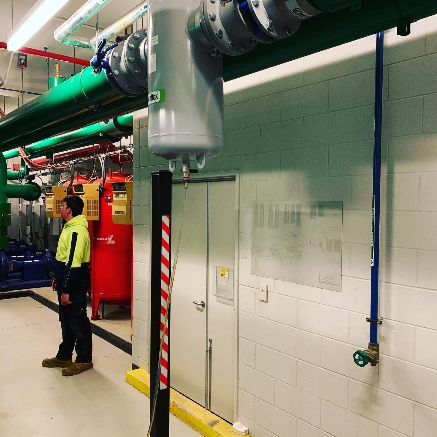 Man in Safety Vest Stands in Utility Room with Pipes and Equipment — Leader Air Conditioning in Queanbeyan, NSW