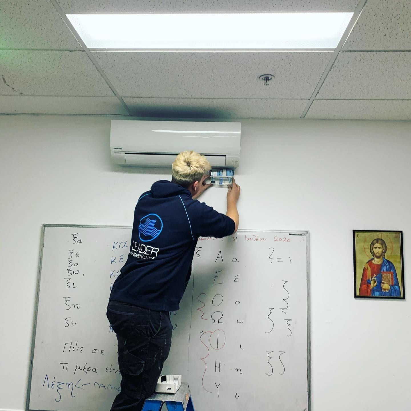 Person On Stepladder Working on Wall-Mounted AC Unit Above Whiteboard — Leader Air Conditioning in Goulburn, NSW