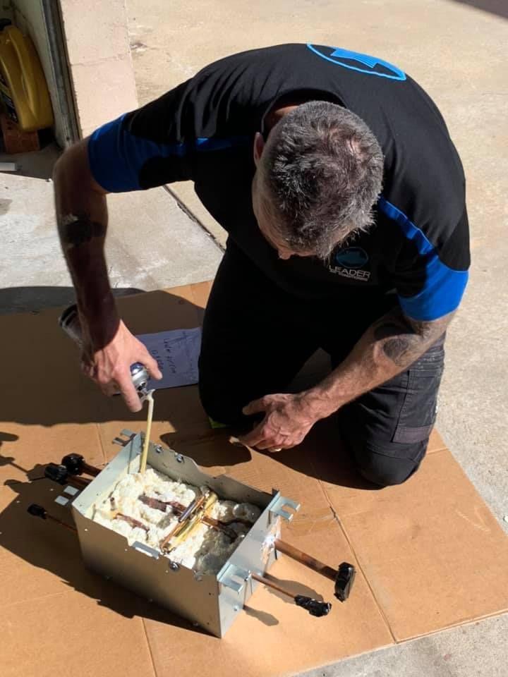 Man kneeling, applying sealant to a metal object on cardboard outdoors. — Leader Air Conditioning in Queanbeyan, NSW