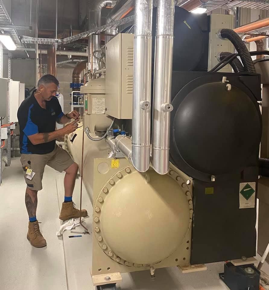 Man in work clothes repairing machinery in an industrial setting. — Leader Air Conditioning in Queanbeyan, NSW