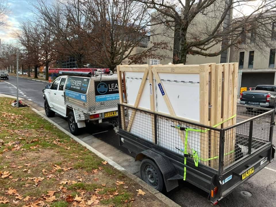 White truck towing a trailer carrying a large, wooden-framed object, parked on the street. — Leader Air Conditioning in Queanbeyan, NSW