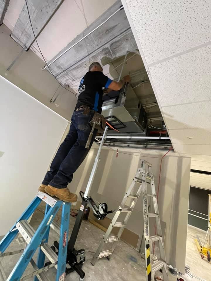 Man on Ladder Working on Ceiling Ventilation in A Construction Site — Leader Air Conditioning in Queanbeyan, NSW