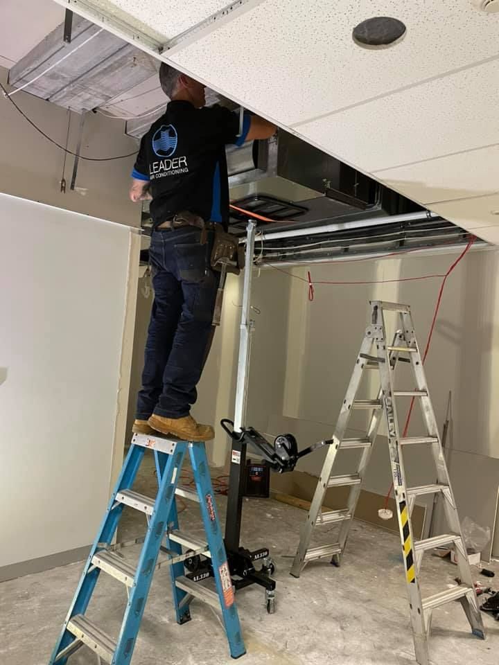Man on ladder installing ceiling component, with another ladder and lift in room. — Leader Air Conditioning in Yass, NSW