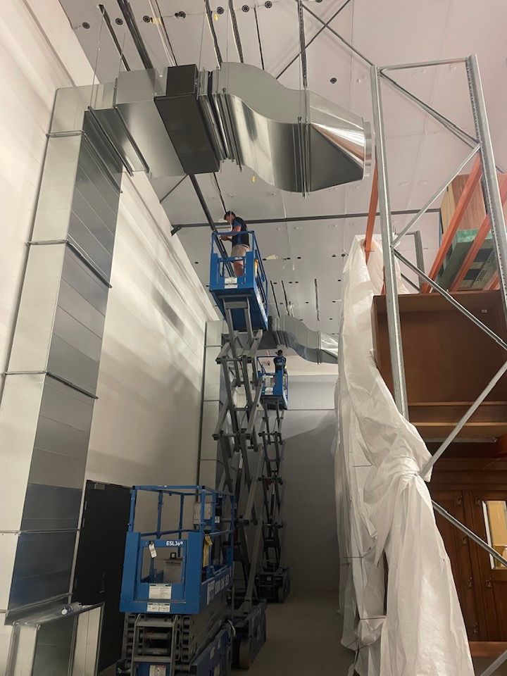 Workers on scissor lifts installing HVAC ductwork in a high-ceilinged room. Silver metal ducts and lifts. — Leader Air Conditioning in Queanbeyan, NSW