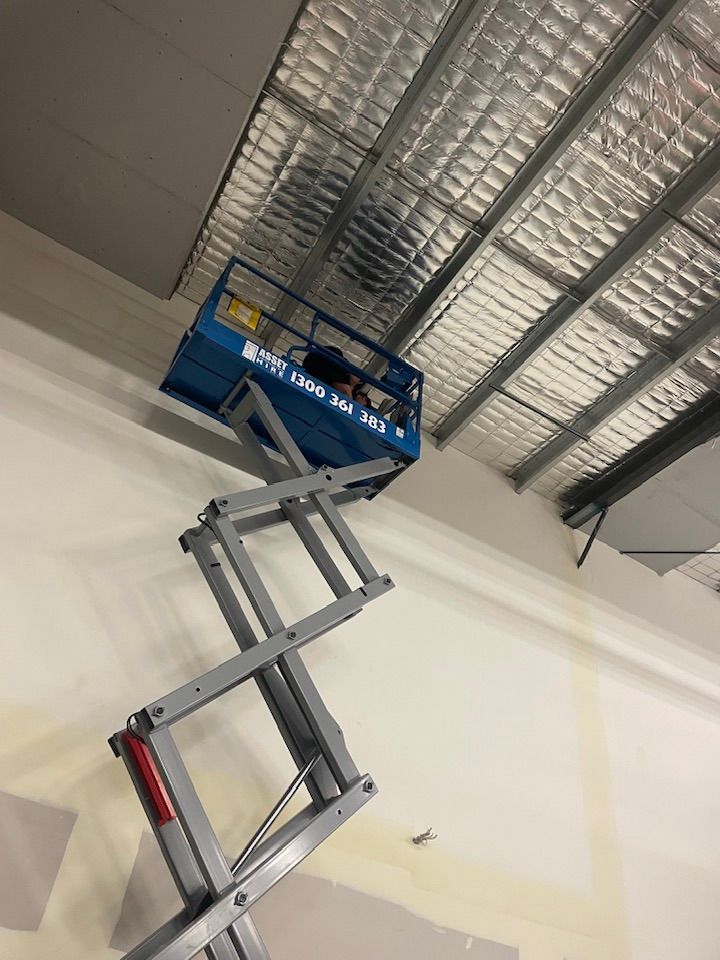 Blue scissor lift raised near a ceiling. Silver insulation and support beams are visible overhead. — Leader Air Conditioning in Queanbeyan, NSW