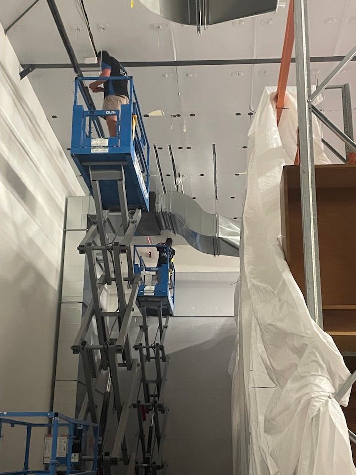 Two workers on a scissor lift installing ceiling fixtures in a construction setting. — Leader Air Conditioning in Yass, NSW