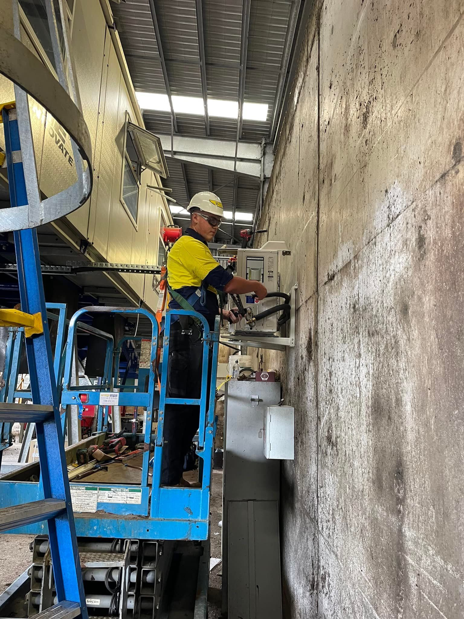 Person on Lift Working on Equipment Next to A Wall — Leader Air Conditioning in Goulburn, NSW