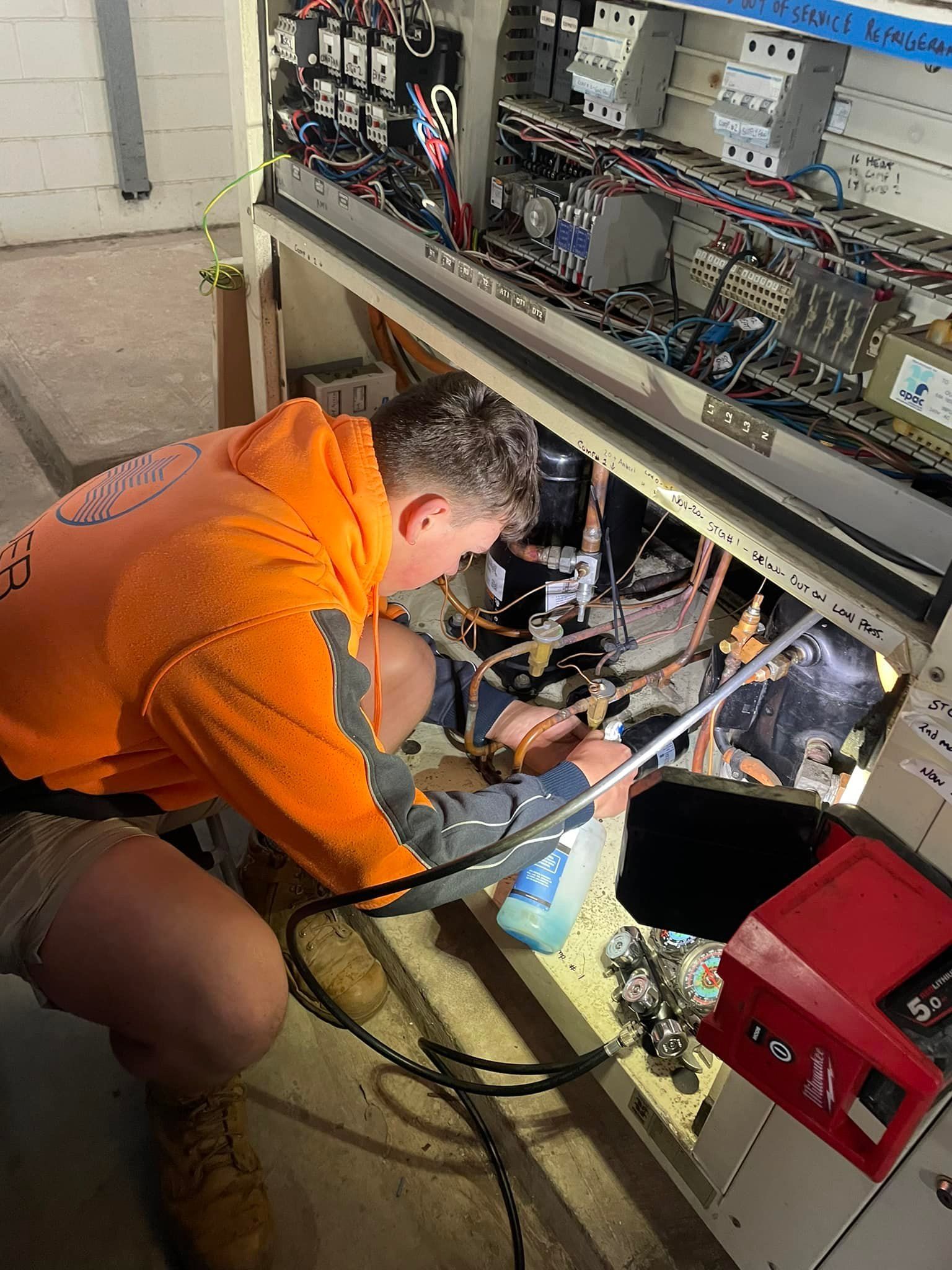 An Electrician in Orange Shirt Repairs Electrical Panel — Leader Air Conditioning in Goulburn, NSW
