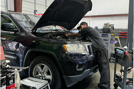 Mechanic working on a black SUV engine with the hood open in a garage. | Jeremi's Auto Repair