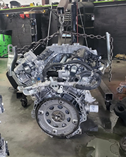 Engine suspended by a chain hoist in a repair shop. Silver metal and black components are visible. | Jeremi's Auto Repair