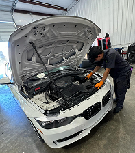 Mechanic inspecting a white BMW with the hood open in a repair shop. | Jeremi's Auto Repair