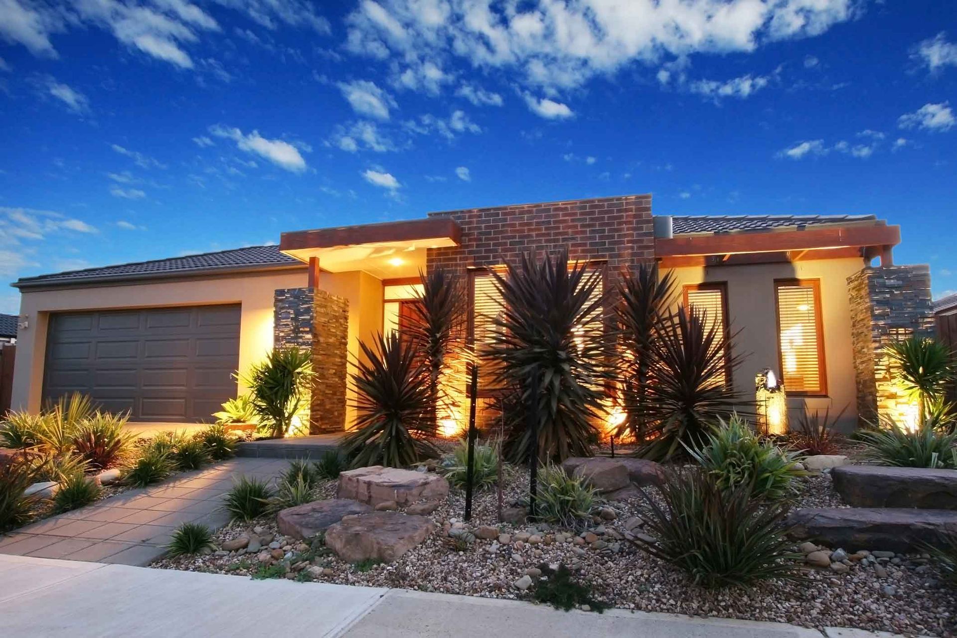 Modern house with stone facade, landscaping, and garage under a blue sky.