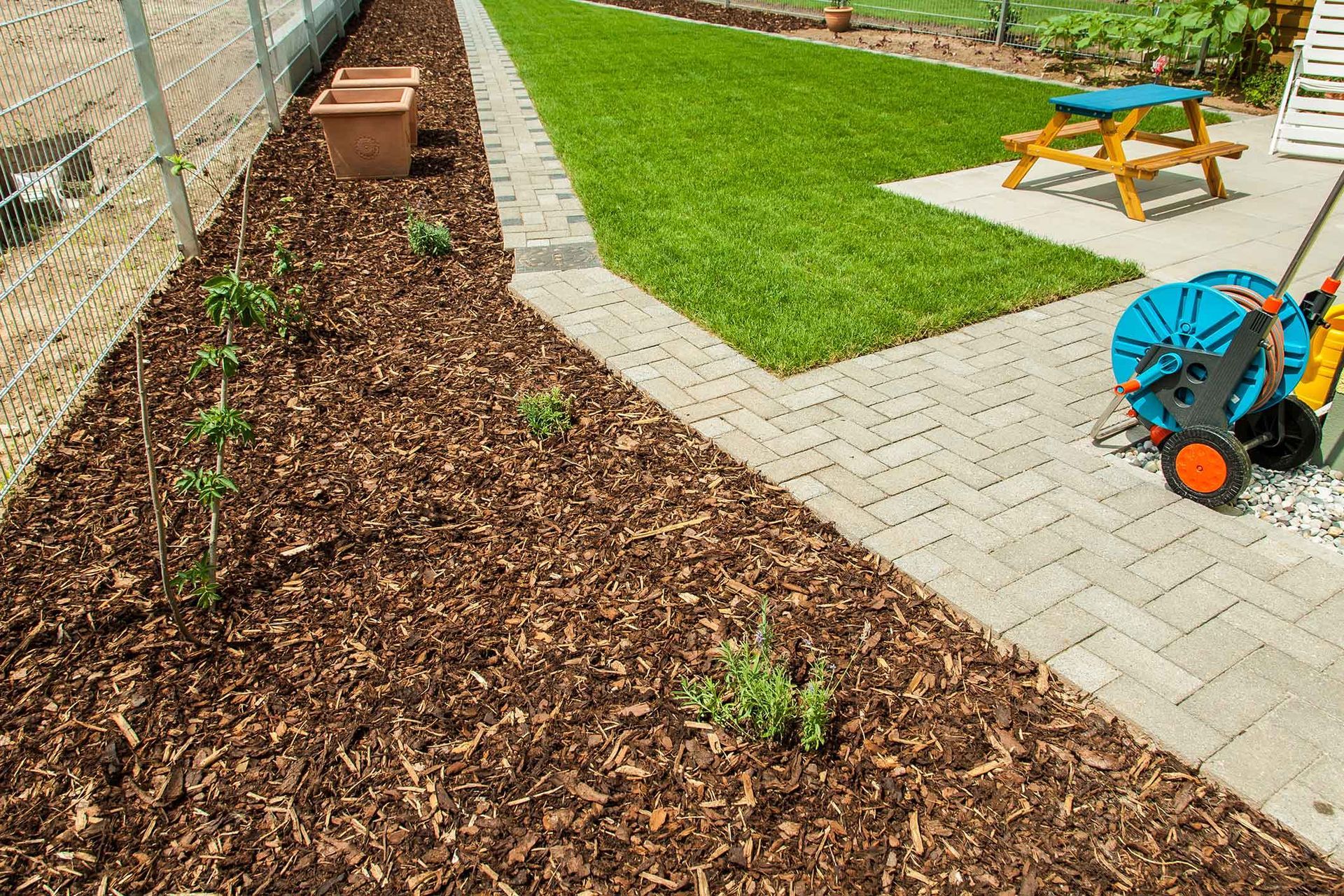 A garden bed with wood chips, plants, and a brick pathway next to a lawn.
