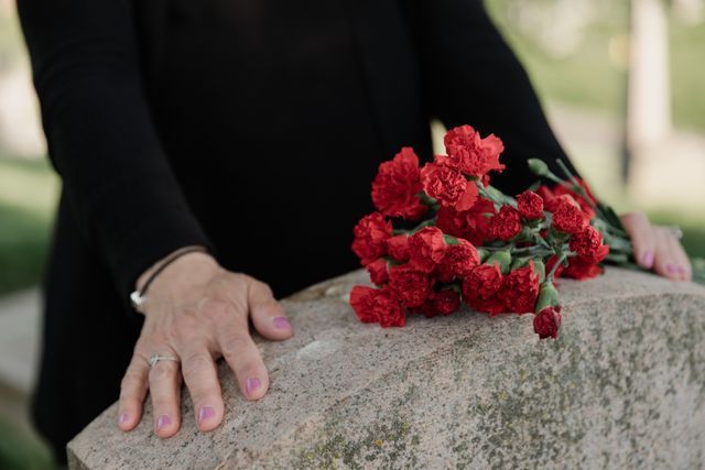 Person standing at a gravesite with red flowers during a memorial service in Hendersonville, TN funeral home and cremations setting