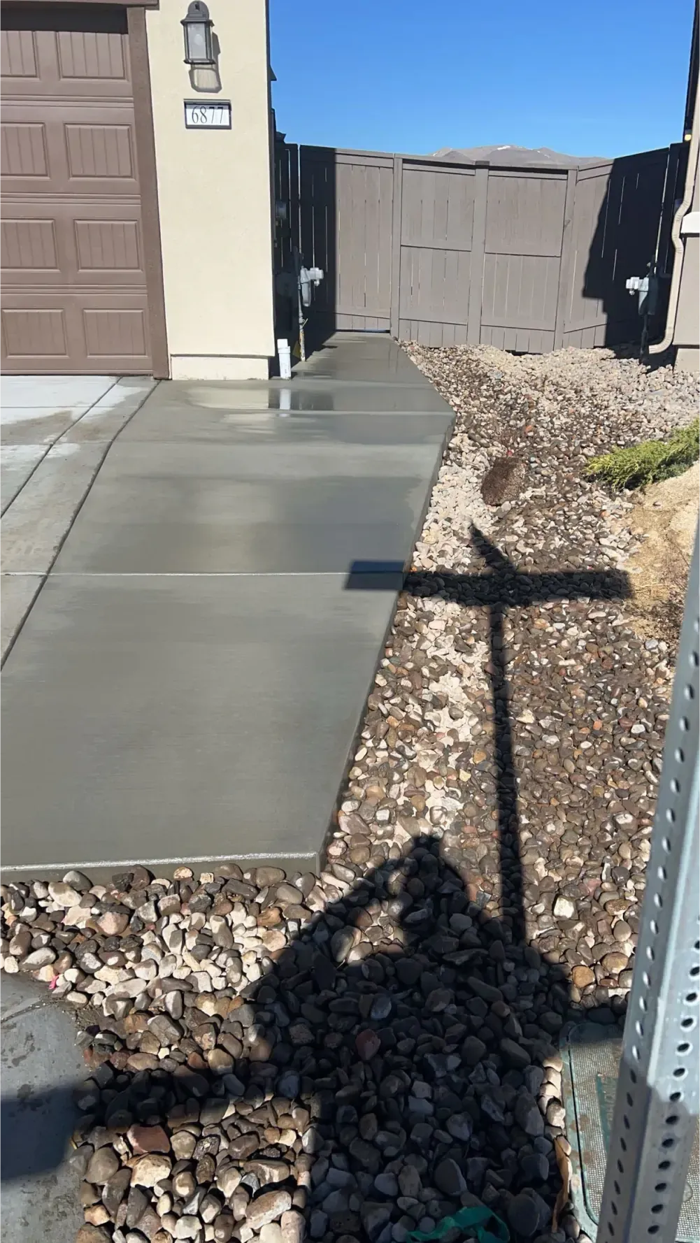 A shadow of a person is cast on a concrete sidewalk in front of a house.