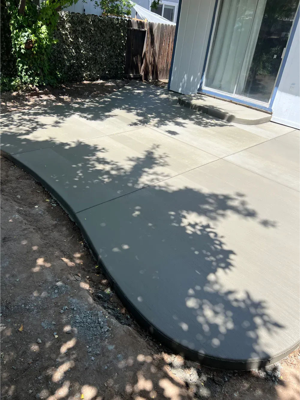 A concrete patio is being built in the backyard of a house.
