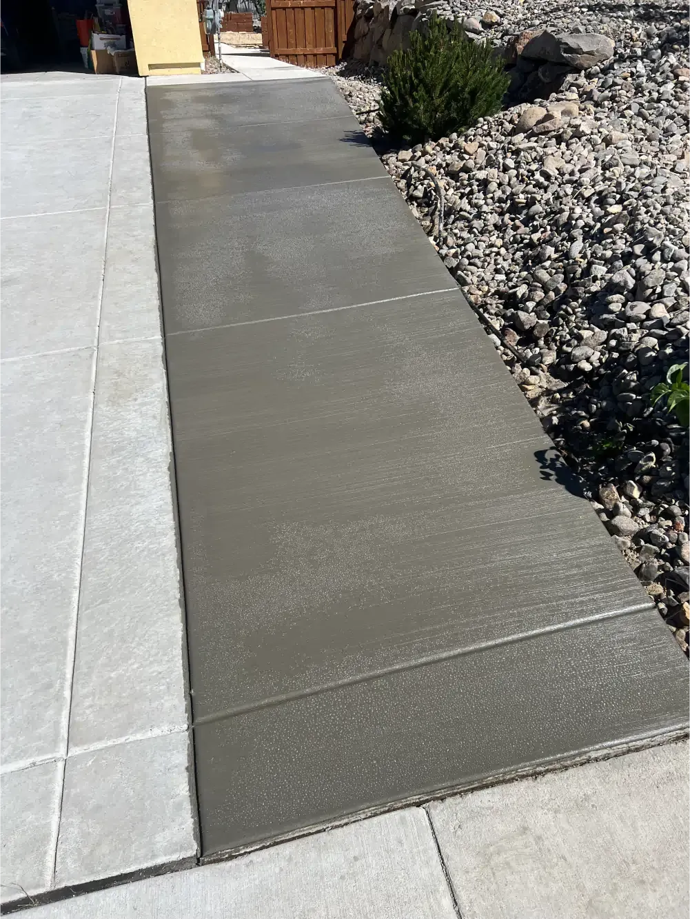 A concrete walkway leading to a garage next to a rocky area.