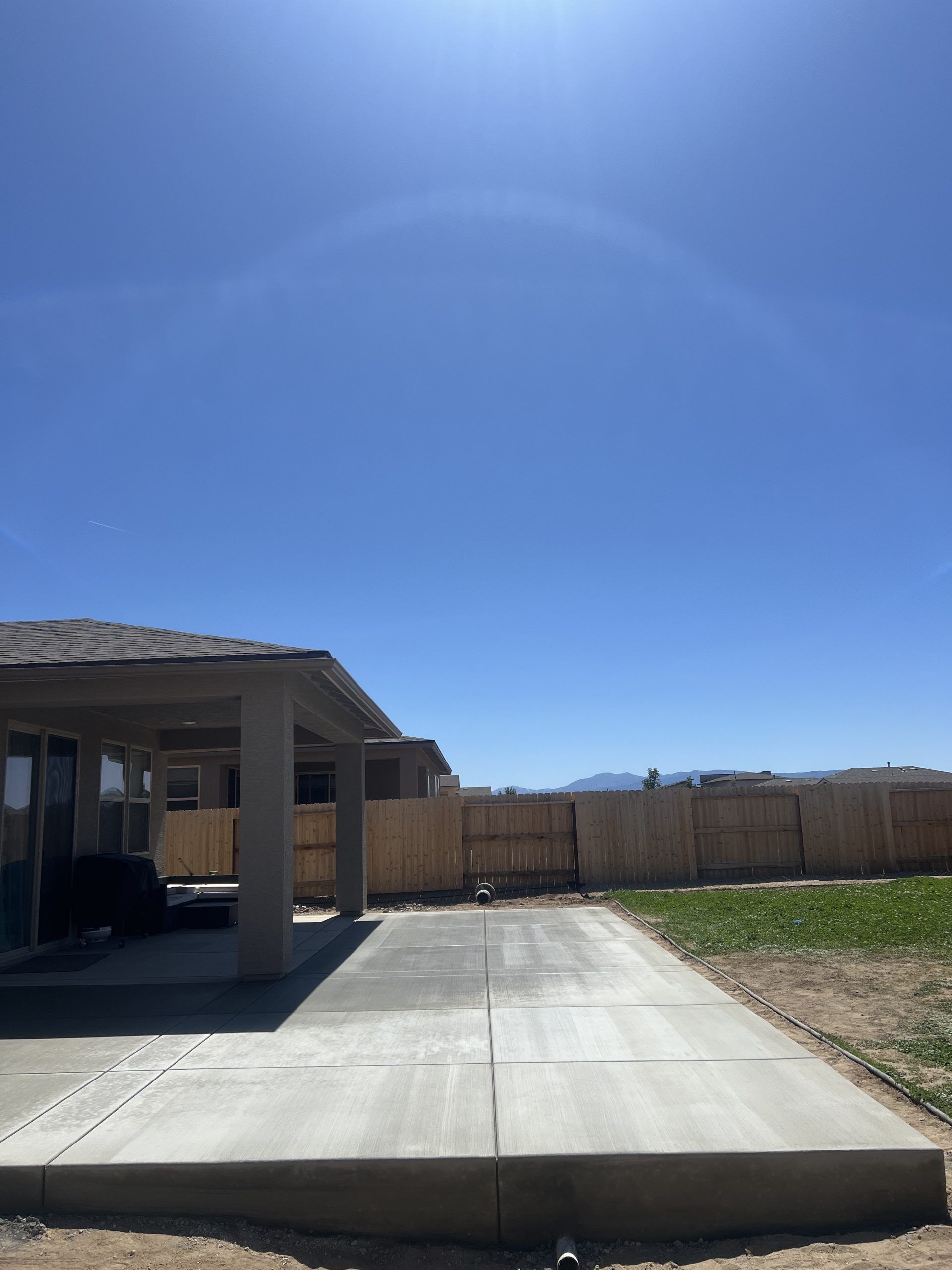 A concrete driveway leading to a house with a wooden fence in the background