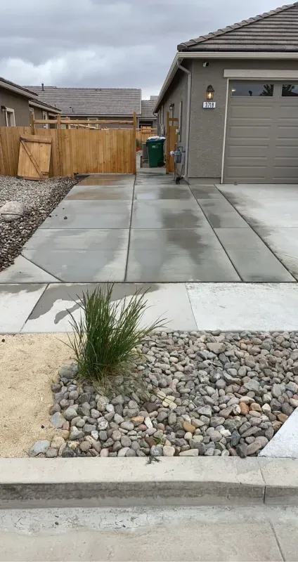 A concrete driveway leading to a house with a wooden fence.